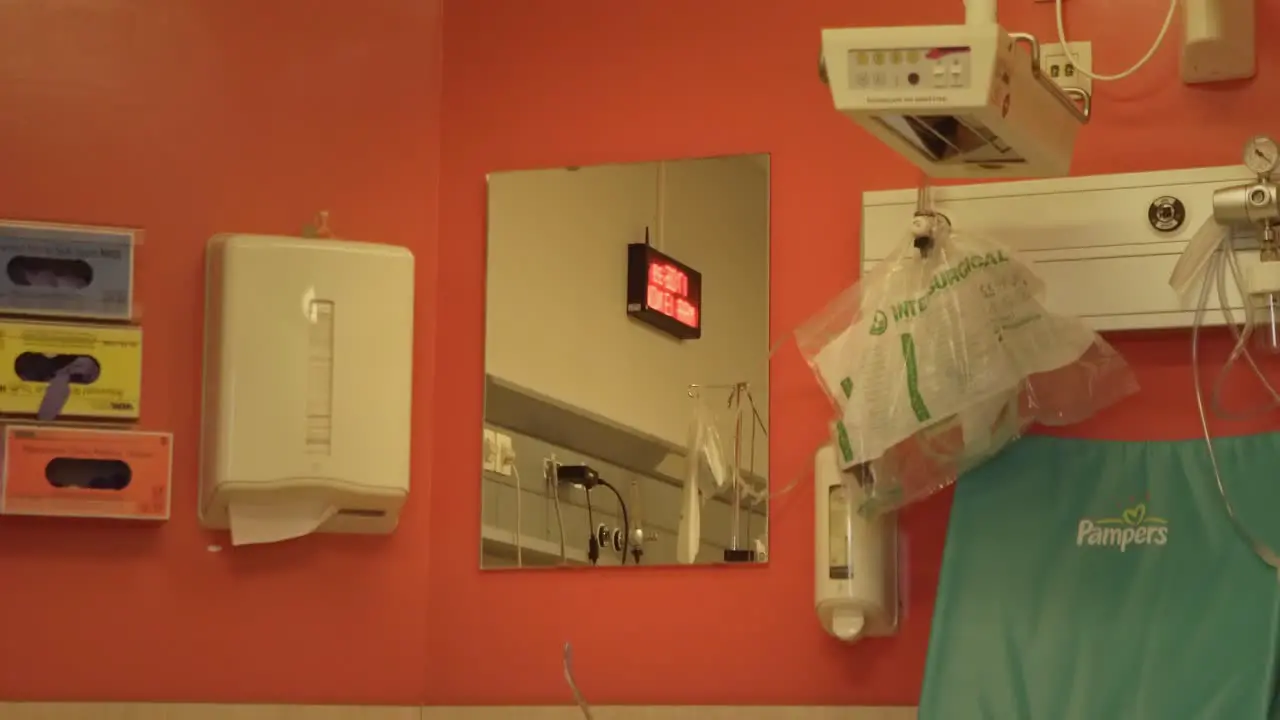 Hospital mirror with a clock reflection on an orange wall with tissues and baby equipment