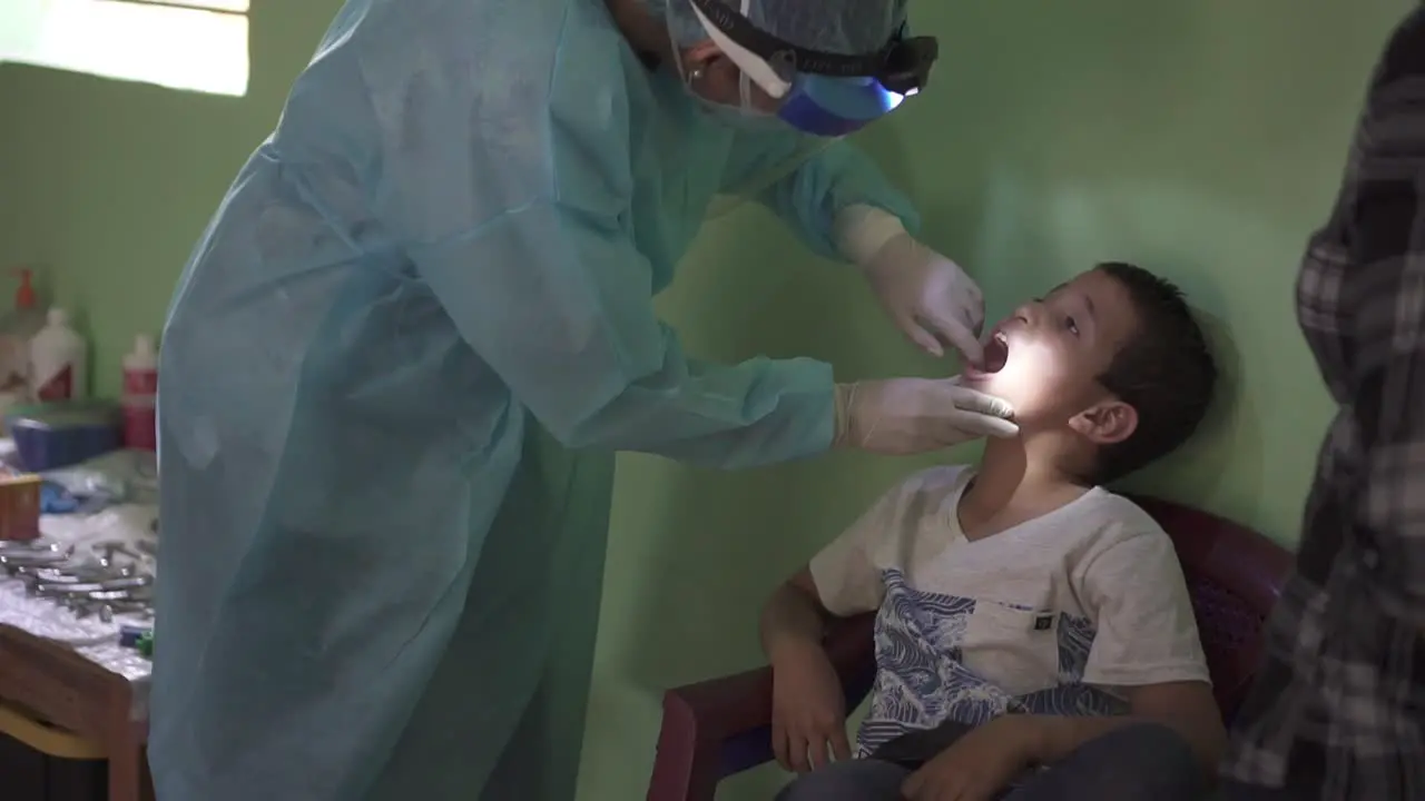 Dentist woman checking the mouth and teeth of a child during a medical brigade in an improvised clinic in a poor community school