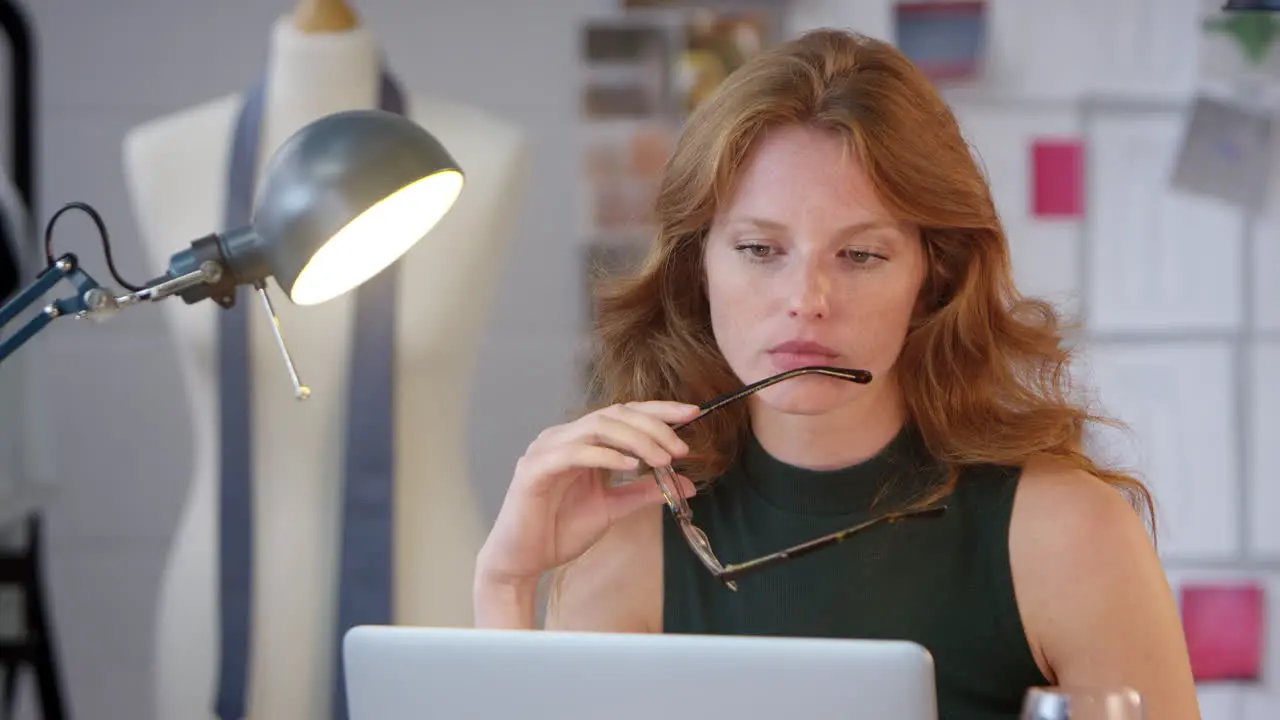 Tired Female Owner Of Fashion Business With Glass of Wine Working Late On Laptop In Studio