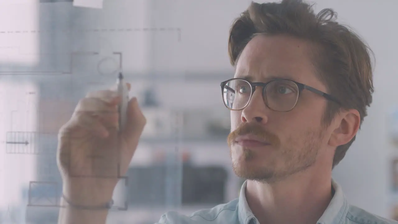 Male Architect In Office Making Notes On Building Blueprint On Transparent Screen