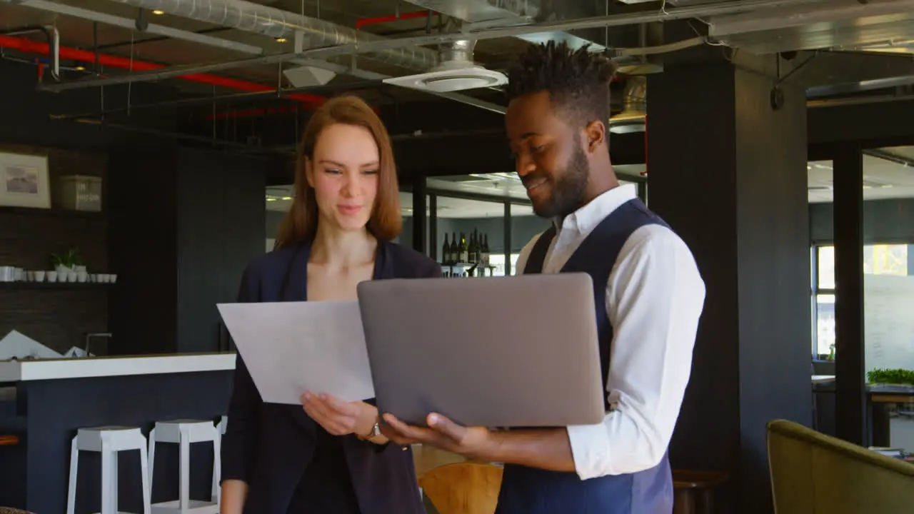 Front view of young cool mixed-race business team planning and holding laptop in modern office 4k