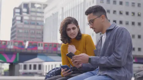 Arc Shot of Two Students Talking and Using Smartphone with City Backdrop