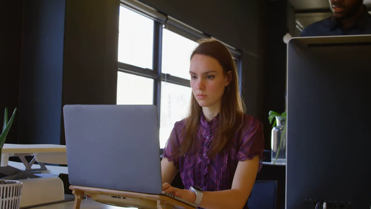 Front view of young caucasian businesswoman working on laptop at desk in a modern office 4k