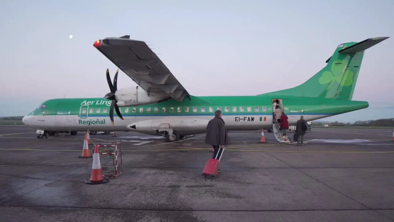 Close wide shot of people boarding an Aer Lingus airplane in Cork Ireland at dawn with moon in the background