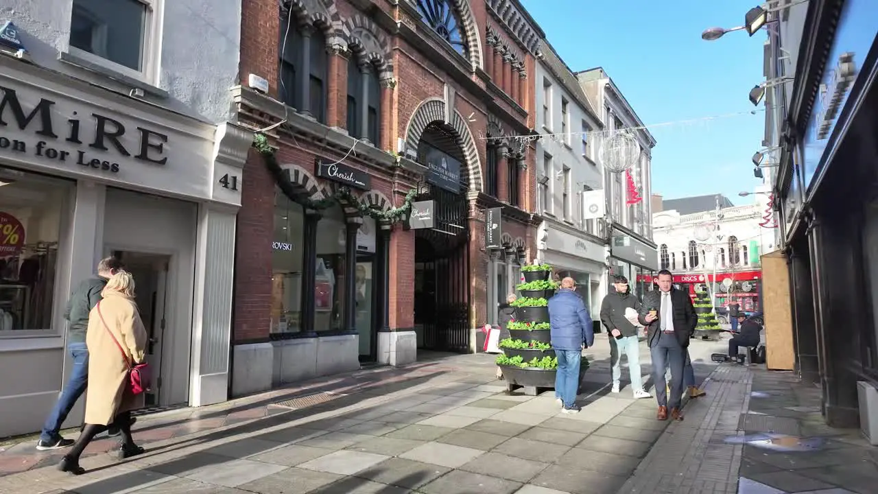 Pedestrians in winter coats and jackets with coffee mug in slow motion on the street of Cork City Ireland sunny morning