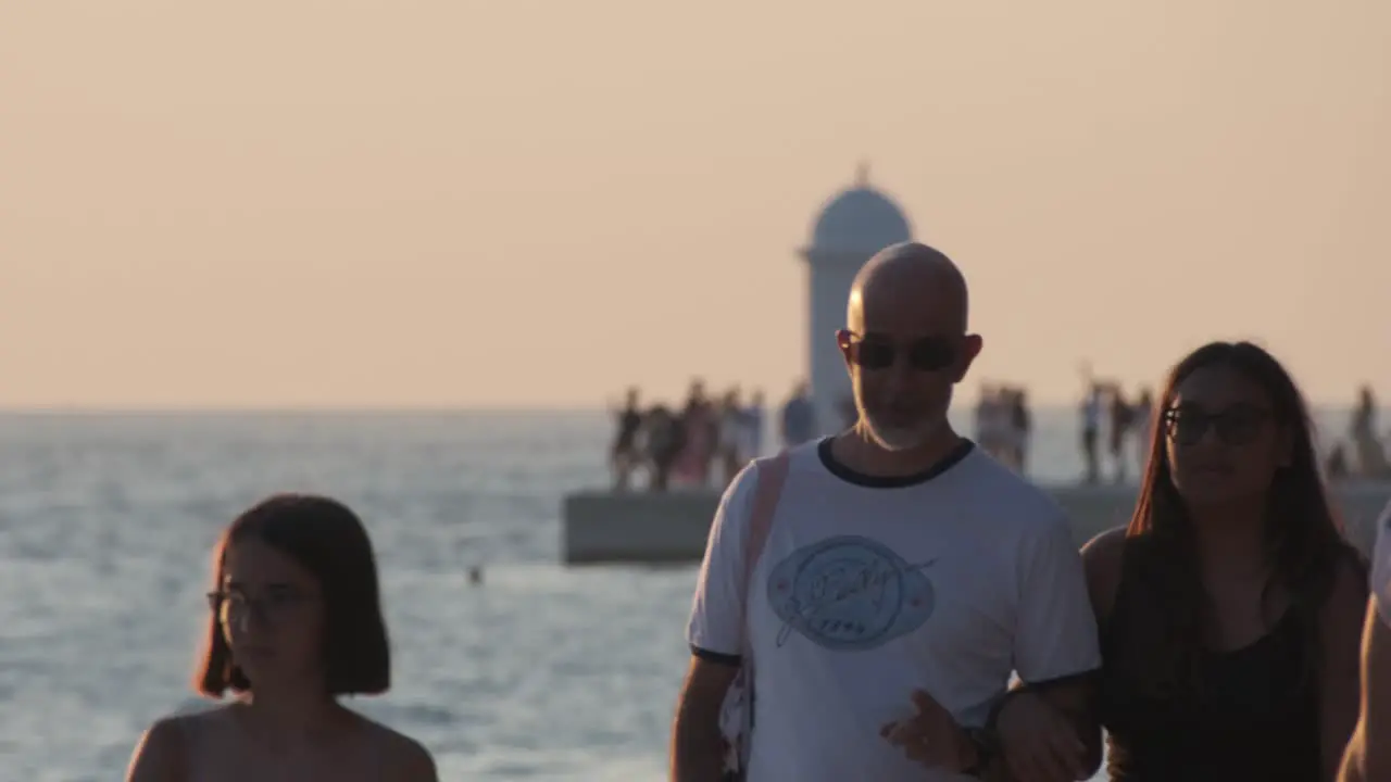 People walking Zadar promenade at sunset with lighthouse and more people in background