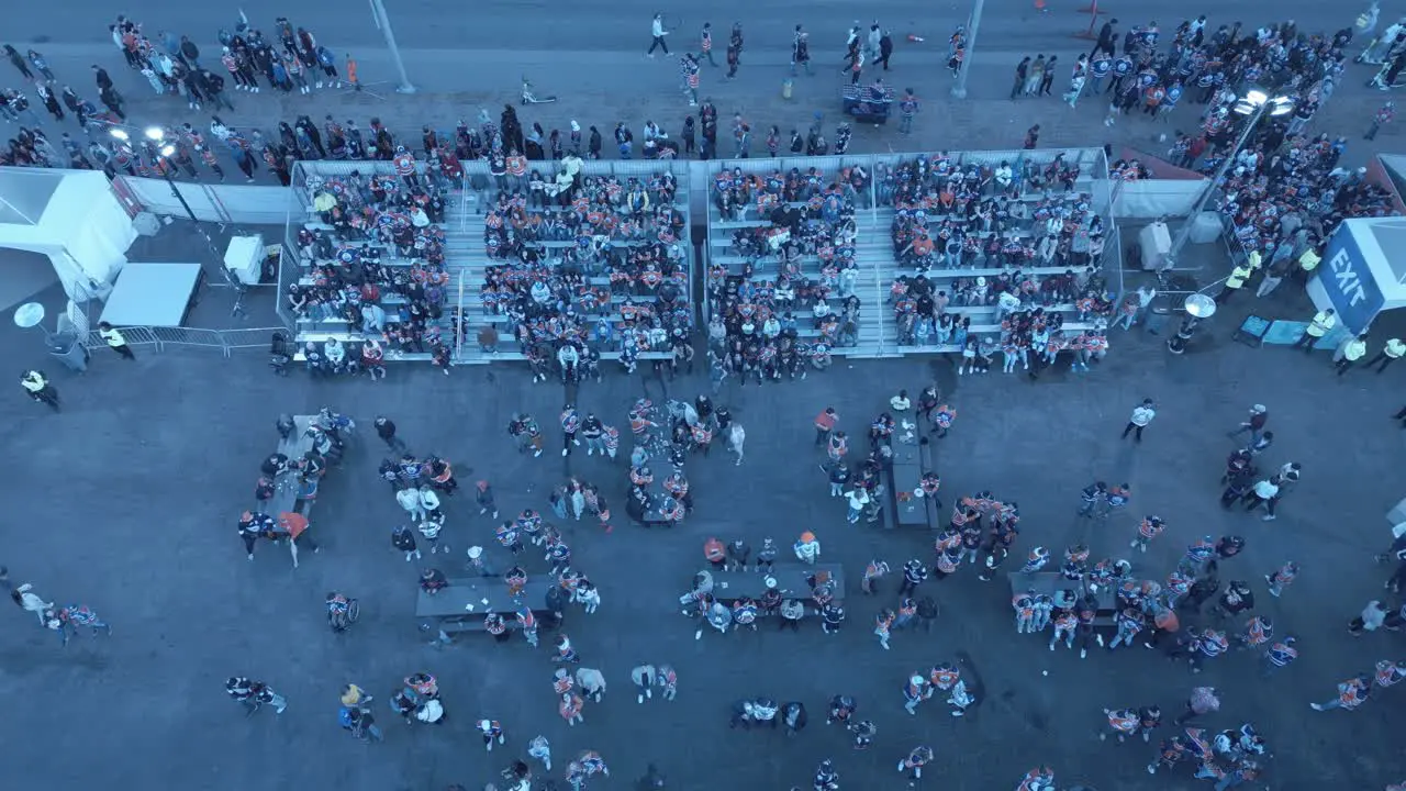 Aerial drone hold overlooking crowds of people cheering waving at camera on bleachers outside free watch party next to Rogers Place arena at Oilers away game in Edmonton as angry fans await to get in