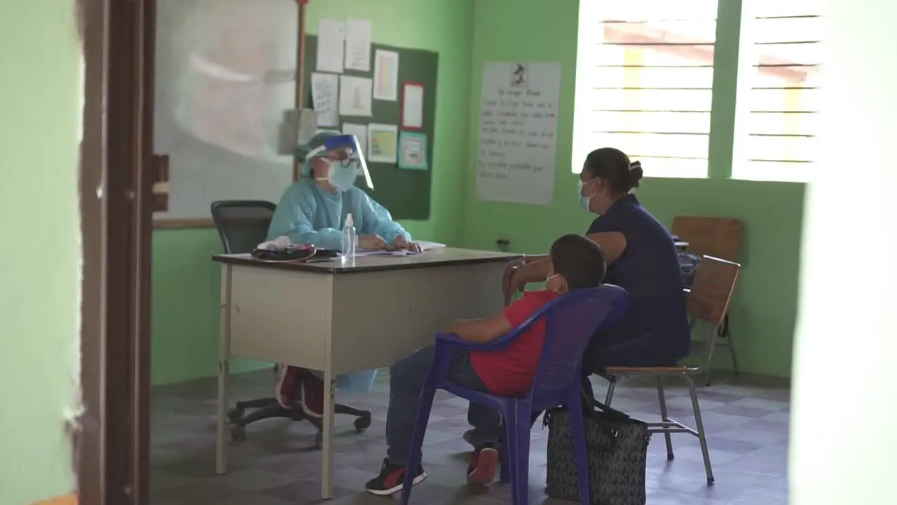 Mother and her son sitting in front of a doctor in a medical consultation during a health brigade in an improvised clinic in a poor community school