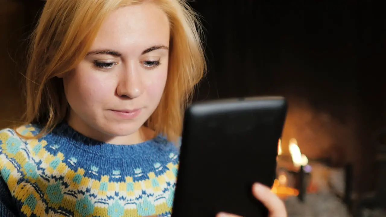 A Young Woman Uses Tablet Near A Christmas Tree On A Background Of Fire 1