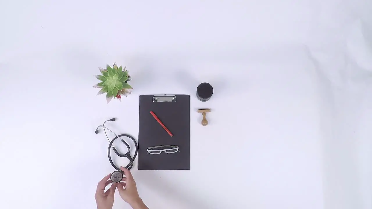 Top-down view of medical items placed on white background with a stethoscope syringe medical glove bandage stickers black dossier folder white glasses notebook and small plants