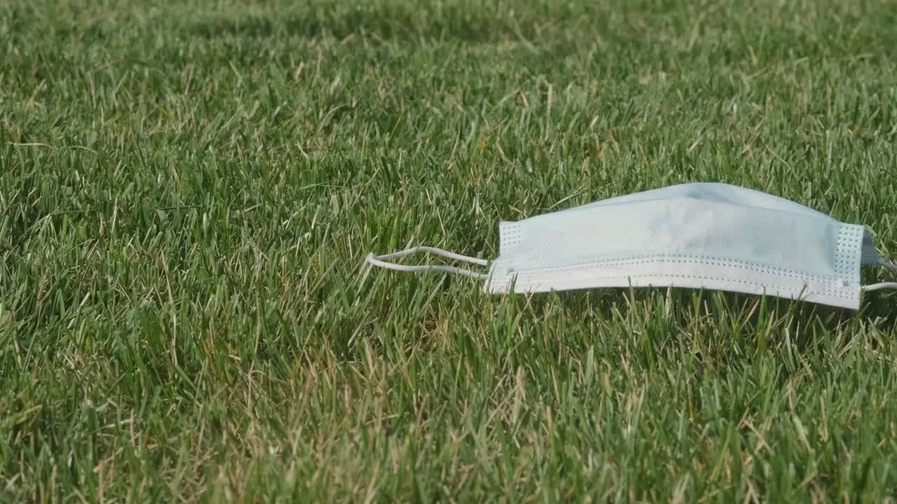 Disposable Surgical Facemask Left On Freshly Cut Green Grass On A Sunny Spring Day