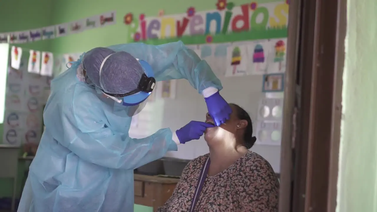 Female dentist cleans the teeth of an adult woman with dental floss during a medical brigade in an improvised clinic in a poor community school