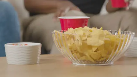 Close Up Of Couple Sitting On Sofa At Home Together Eating Chips And Dips