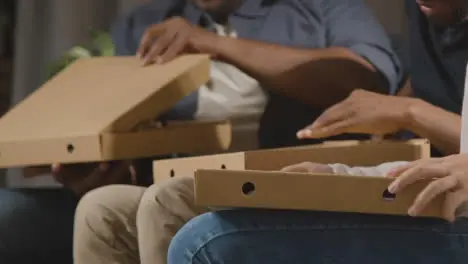 Multi-Cultural Friends Sitting On Sofa At Home Eating Takeaway Pizza Delivery