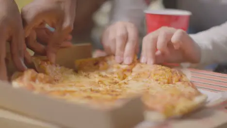 Close Up Of Friends Sitting On Sofa At Home Eating Takeaway Pizza Delivery 