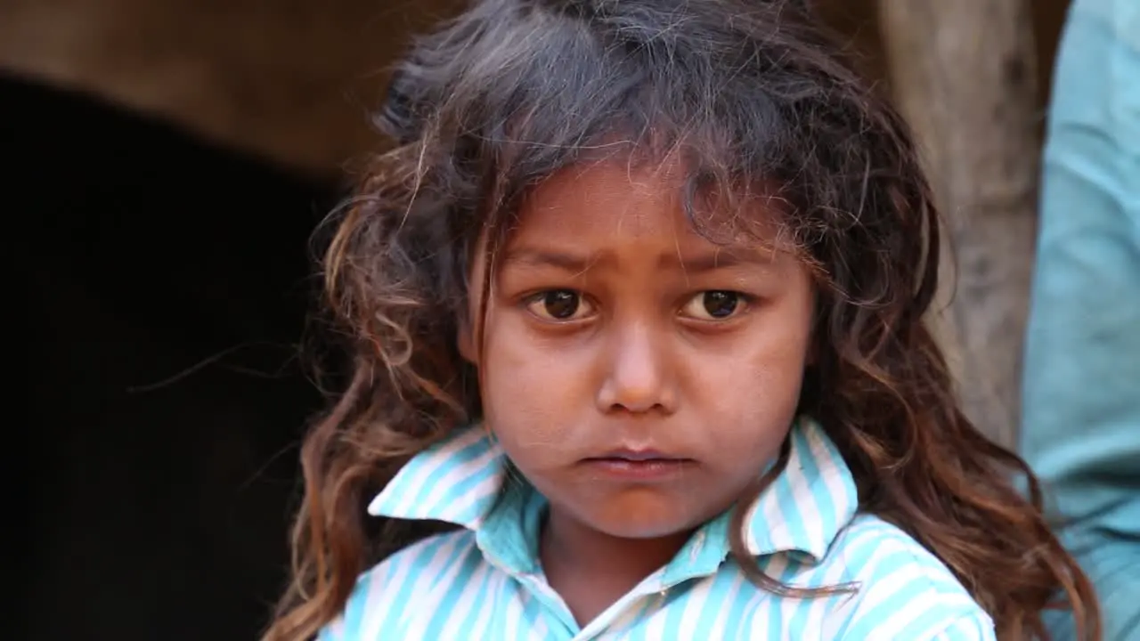 Handheld portrait of unhappy Indian child girl from rural village looking at camera India