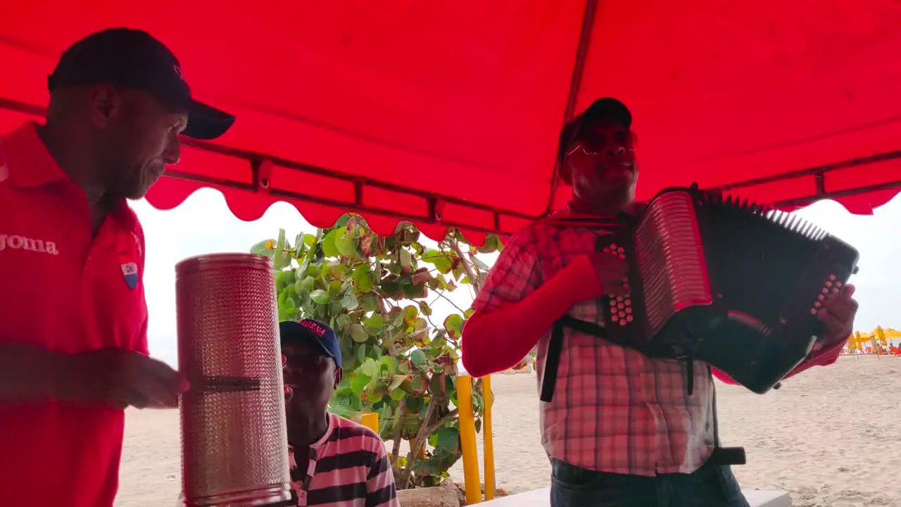 A man is playing the accordion along with his fellow band members who play the Guacharaca and the caja