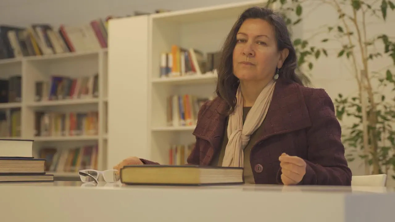 Woman in library takes reading glasses off and looks at camera