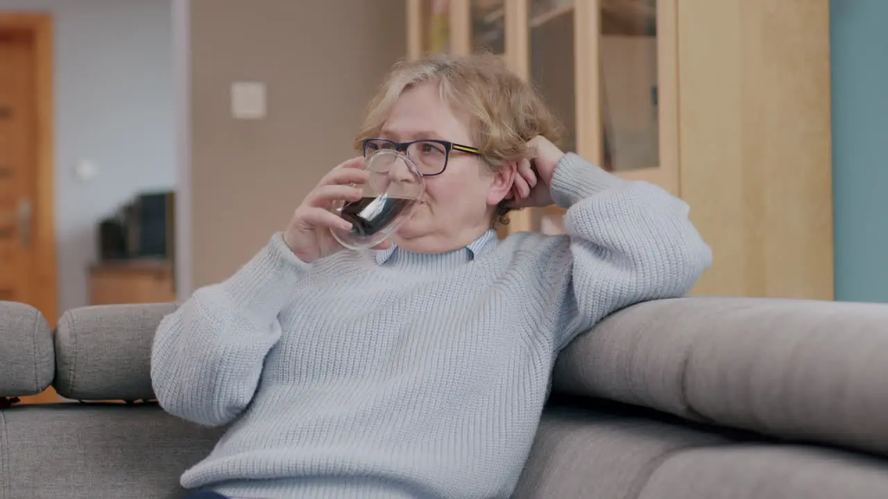 Elderly caucasian woman with glasses relaxes on sofa with a beverage