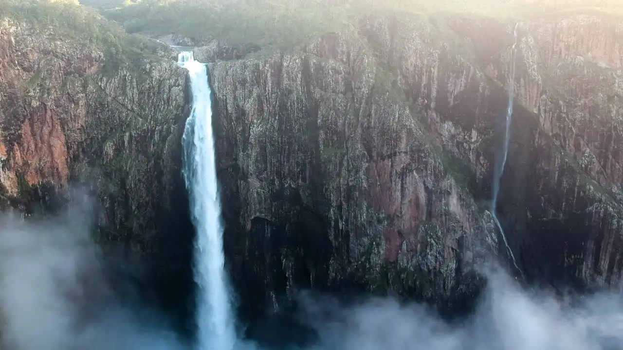 Cinematic drone video from high waterfall droppping water deep on cliffs high mountain australia