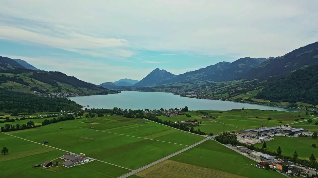 Aerial view of a remote lakefront village surrounded by lush green fields and mountains with a high peak mountaintop in the distance