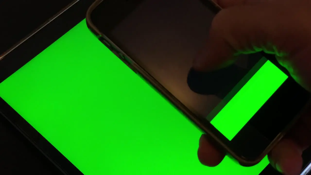 Close up shot of black guy scrolling touchscreen of modern smartphone gadget with green chroma key screen and green tablet in background