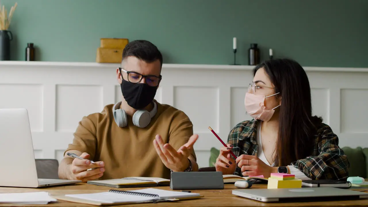 Student With Headphones Talking With Female Mate At Table Discussing About A Project Using Laptop