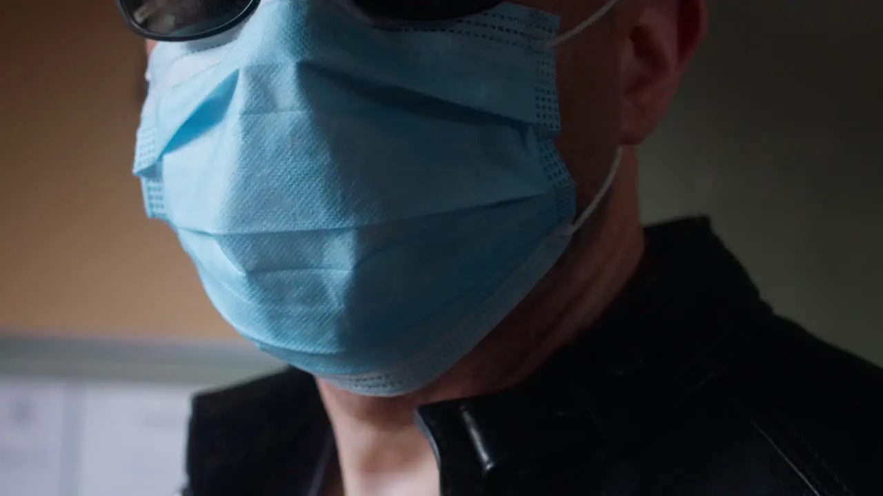 Man wearing a covid-19 surgical mask standing inside looking outside