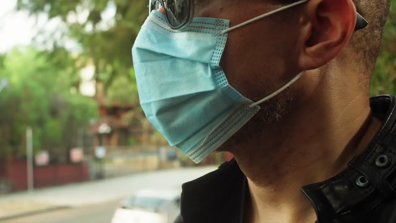 Man standing outside on a sunny day wearing a covid-19 surgical mask and sunglasses