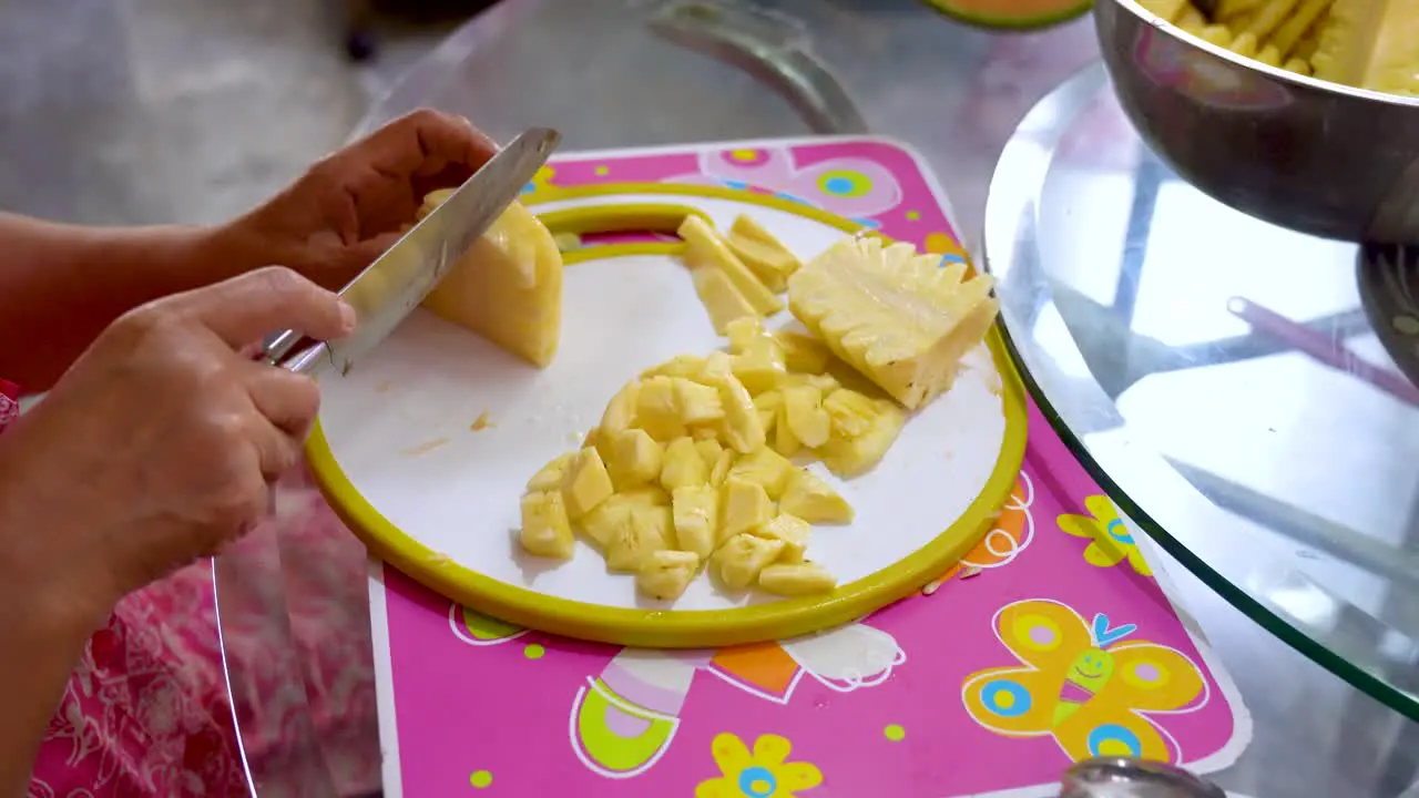 Mother prepares pineapple by slicing for kids to eat close up view