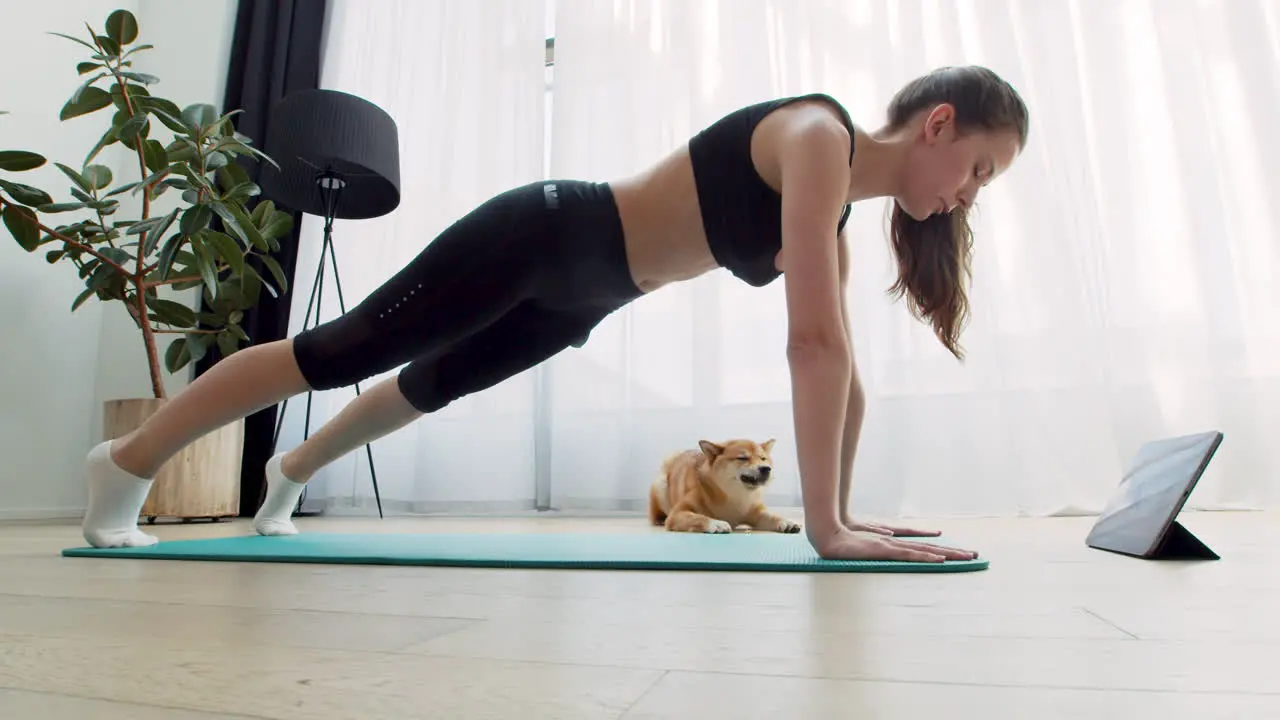 A Cute Girl Does Yoga At Home Next To Her Beautiful Dog