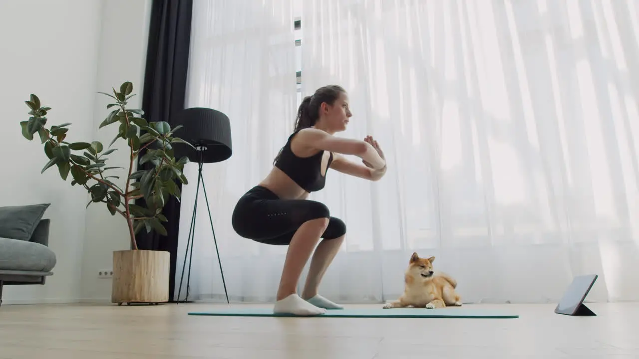 A Young Woman Does Yoga At Home With Her Dog Next To Her 1