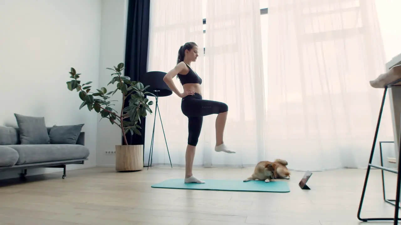 A Young Woman Does Yoga At Home With Her Dog Next To Her