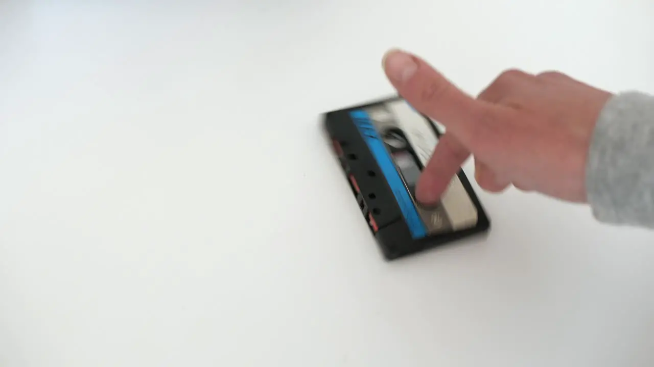 woman spins vintage audio cassette around finger on white surface static