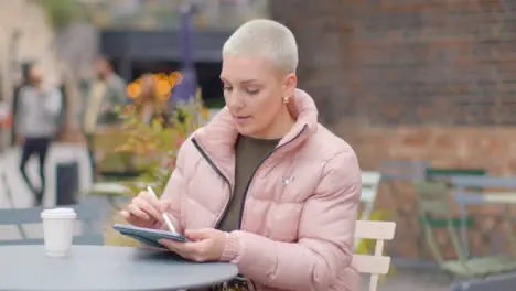 Tracking Shot of Young Woman Sitting at Outdoor Table Sketching On Tablet