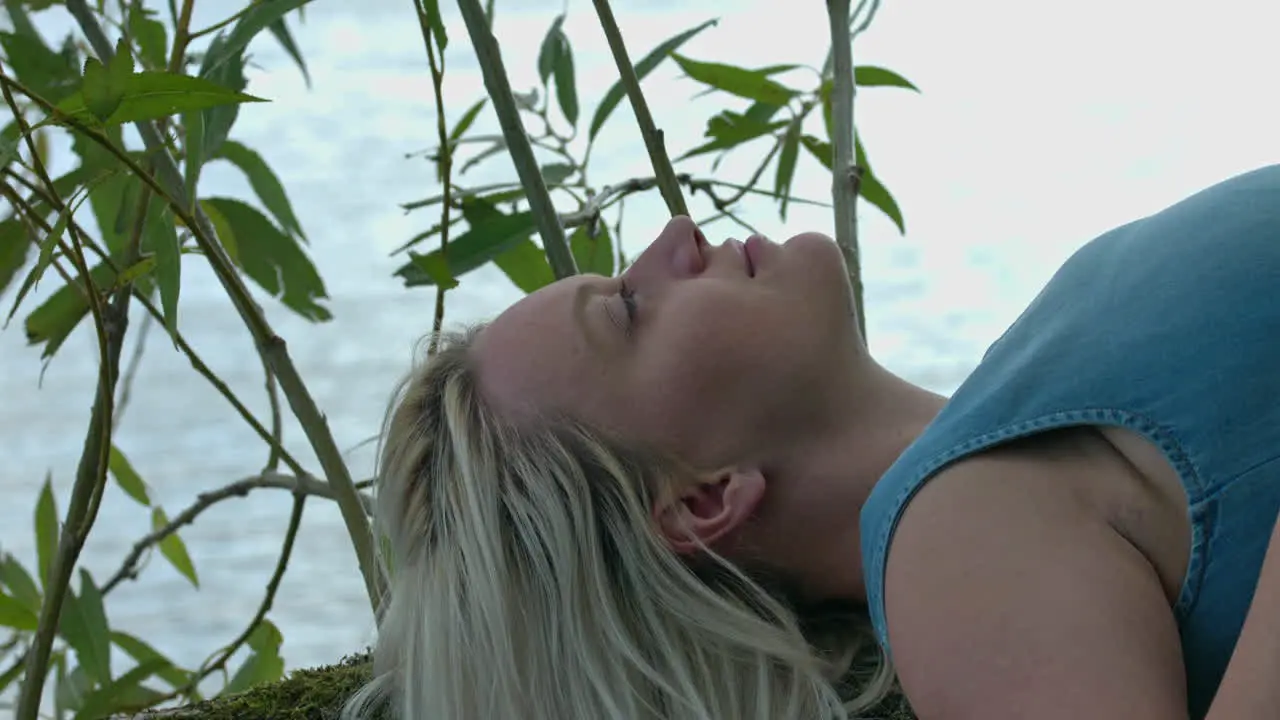 A young woman is lying on her back on a tree branch suspended by the water