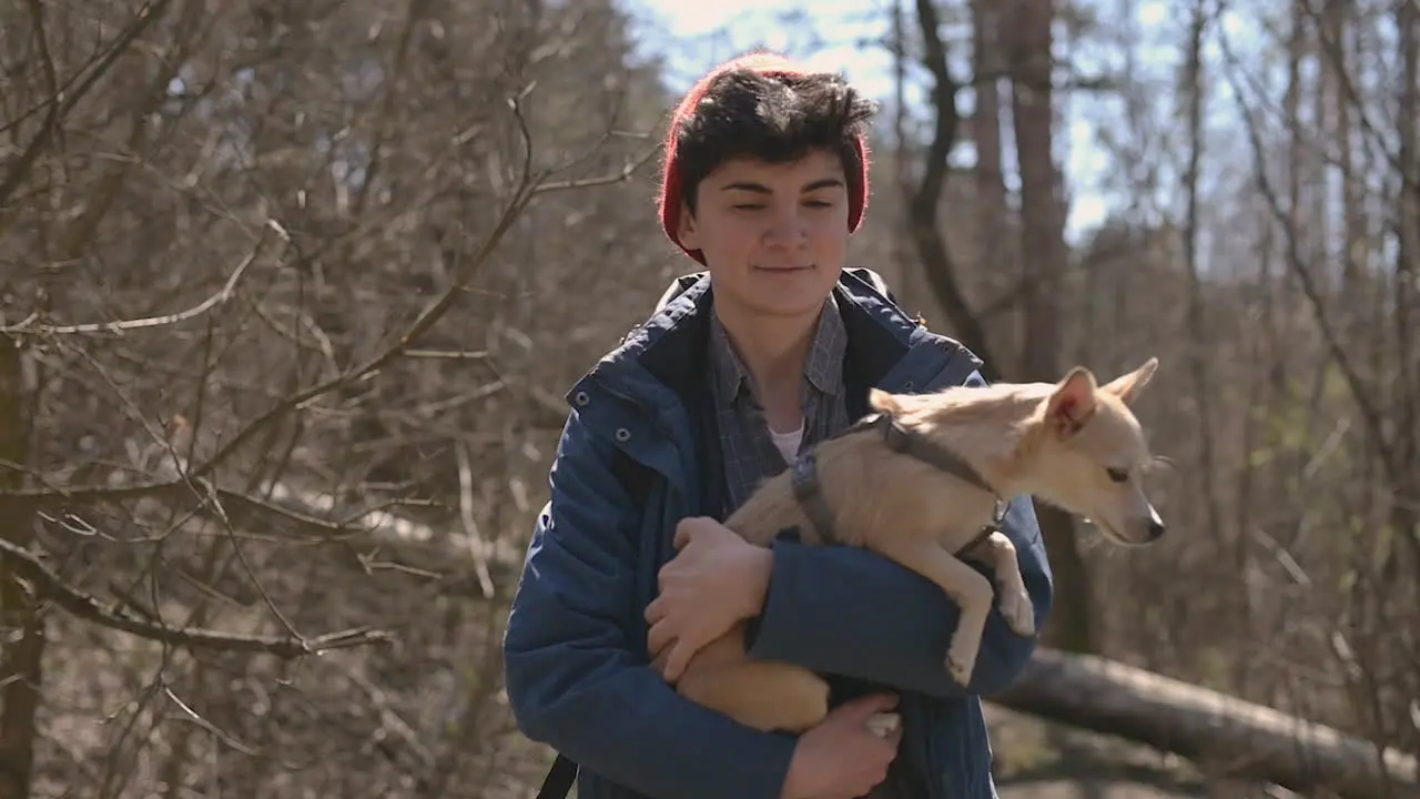 Young Female With Short Hair Takes A Walk In The Forest Holding A Small Dog