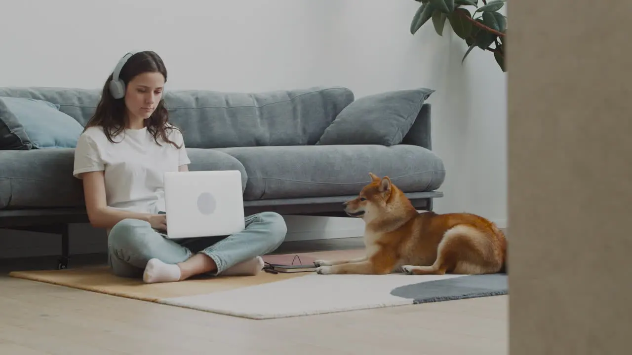 Young Woman Working On Her Laptop At Home Next To Her Dog 1