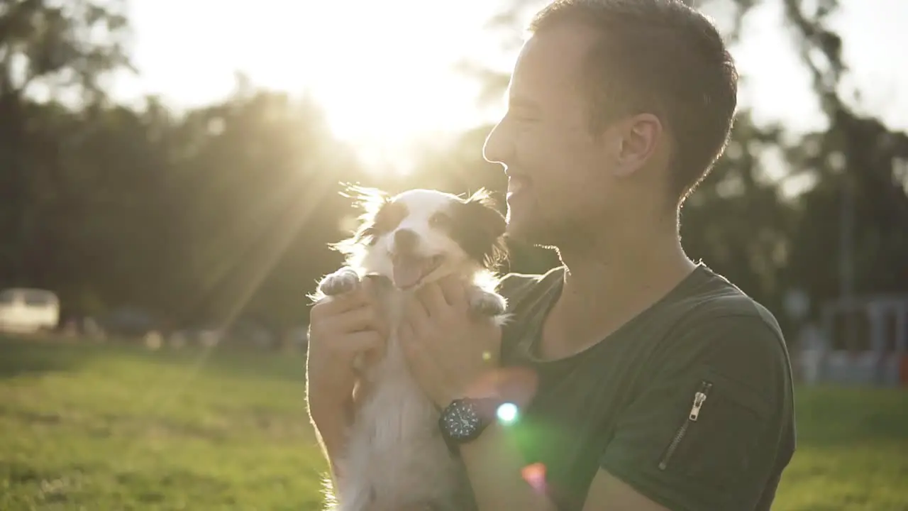 Man Sits On The Grass In The Green Park Play With Young Little Dog