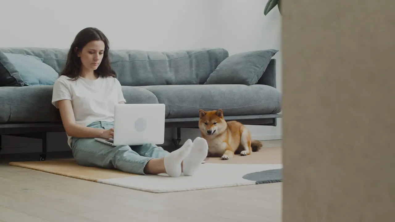 Young Woman Working On Her Laptop At Home Next To Her Dog