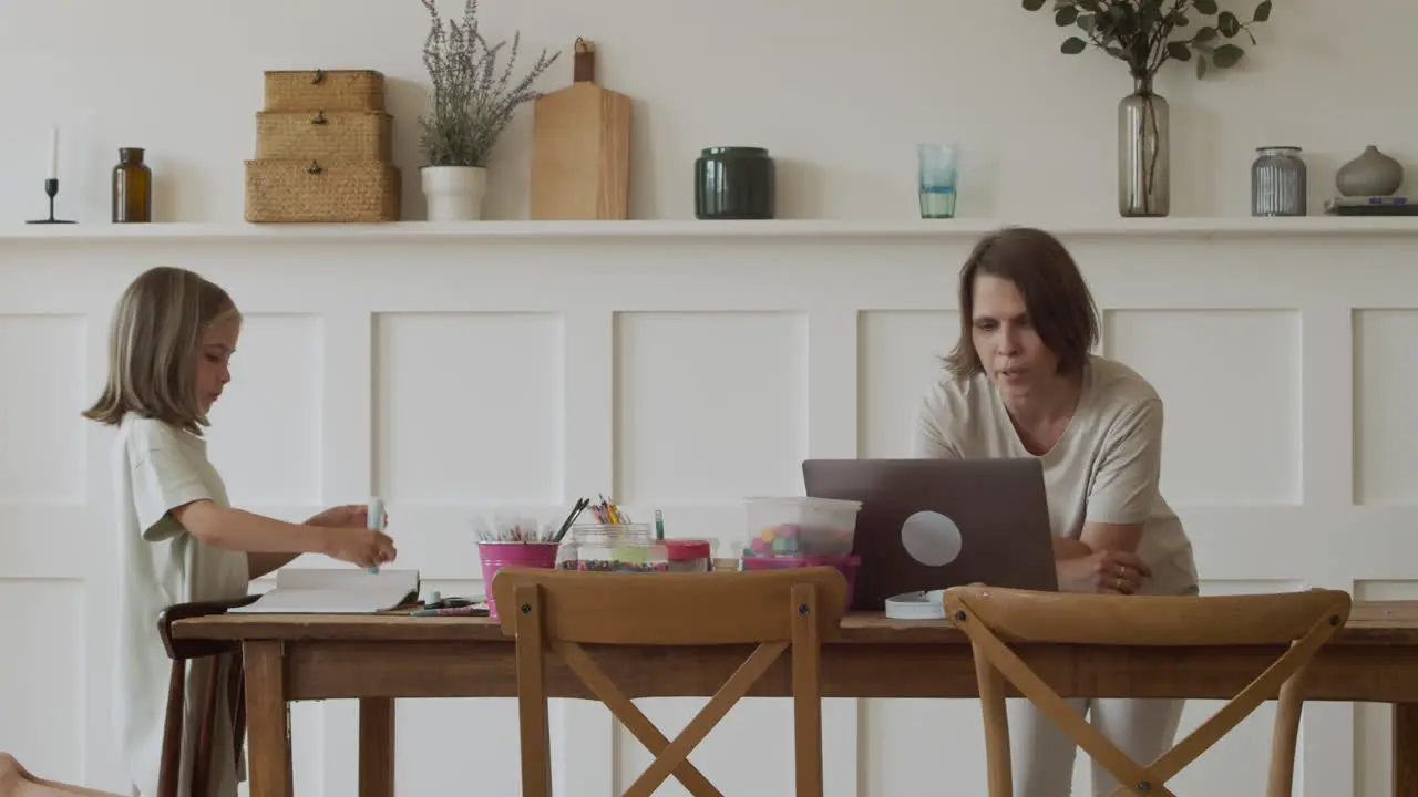 A Mother Makes A Work Video Call At Home With Her Pretty Blonde Daughter While She Does Her Homework