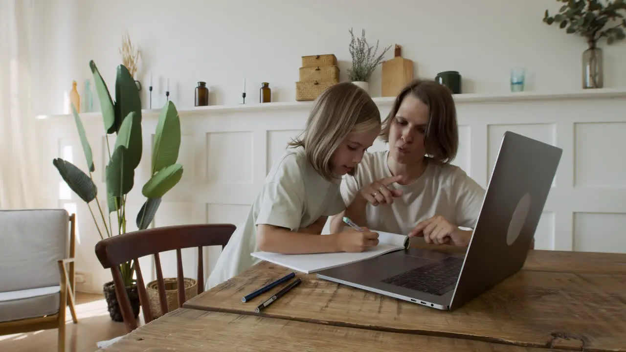 A Cute Blonde Girl Does Her Homework With The Help Of Her Mother While Taking A Look On The Laptop Screen