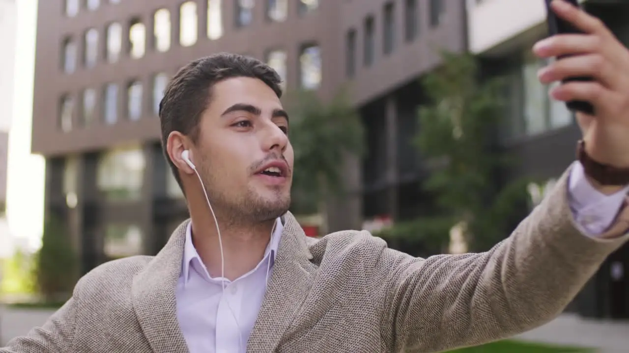 Young Businessman With Earphones Looking At Smartphone Screen During Communication In Urban Environment