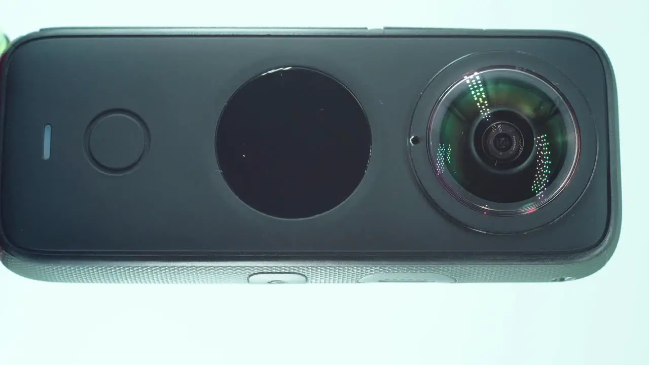 A close up vertical shot of a 360 camera with dual lens two lens covers shiny studio lighting reflecting round screen function button on a rotating stand slow motion 4K video