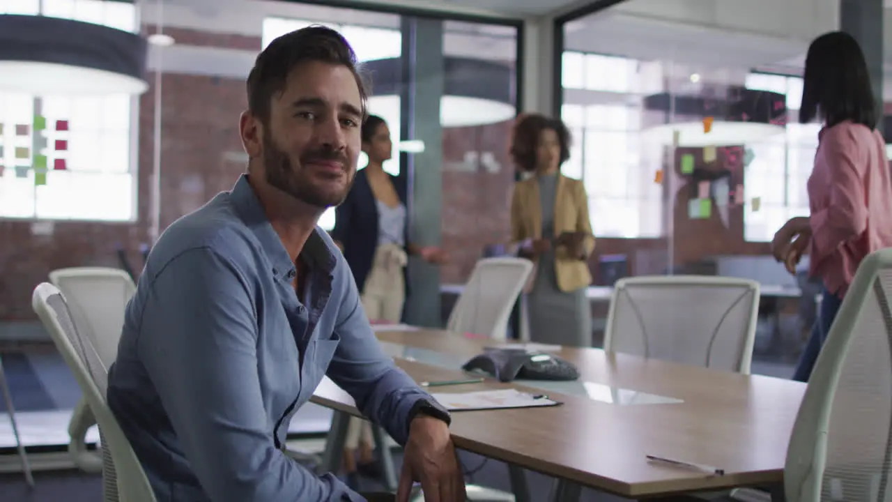 Caucasian businessman sitting smiling in meeting room with diverse colleagues in background