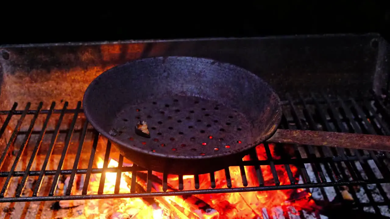 Rusty perforated chestnut cooking roasting pan on opem fire close up dark barckground