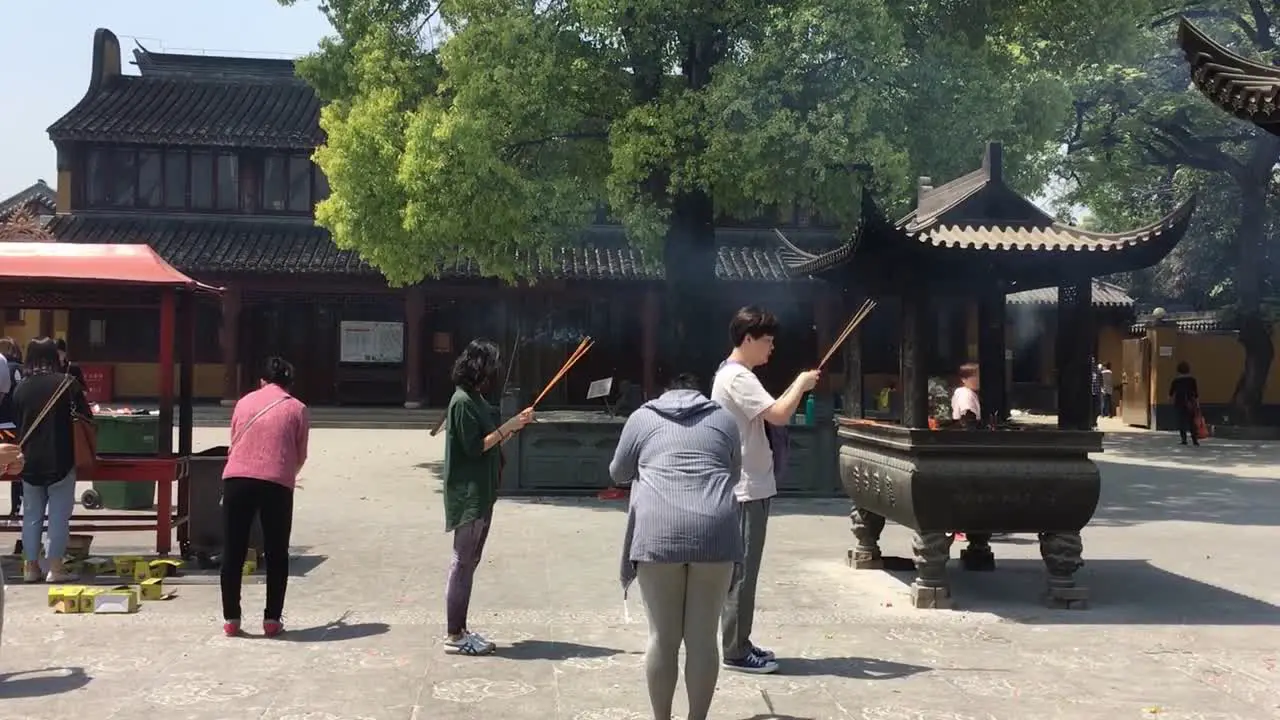 People praying with burning incenses and candles at Longhua Temple in Shanghai China at sunny day