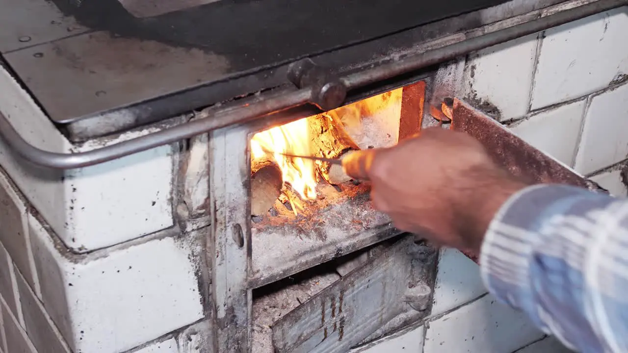 Man uses a poker to level wood and a hearth in a rustic old kitchen stove