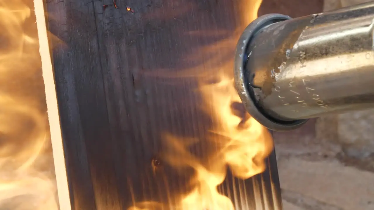 Gas blowtorch burning pine wood plank close up