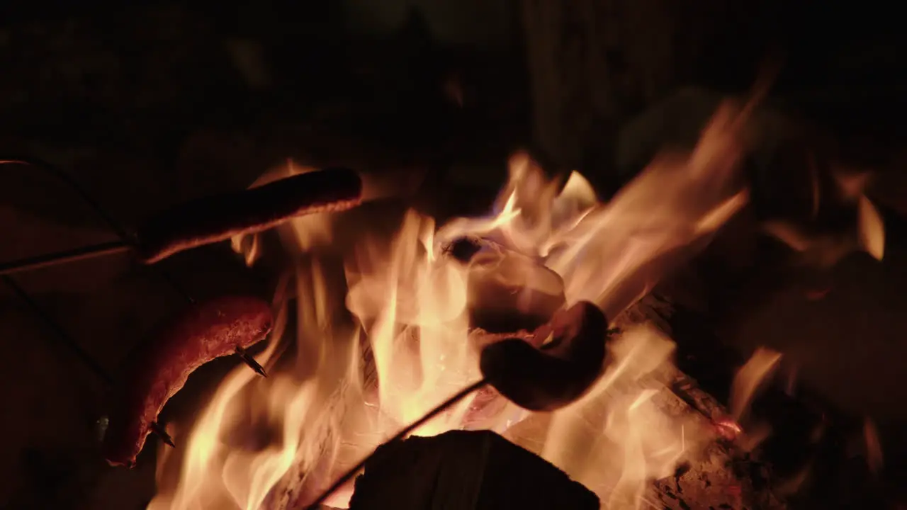 Slow motion close up of campfire with hot dogs being roasted on a stick